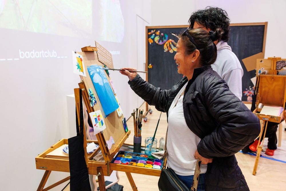 Woman painting on canvas at an easel during an art class workshop with instructor guidance.