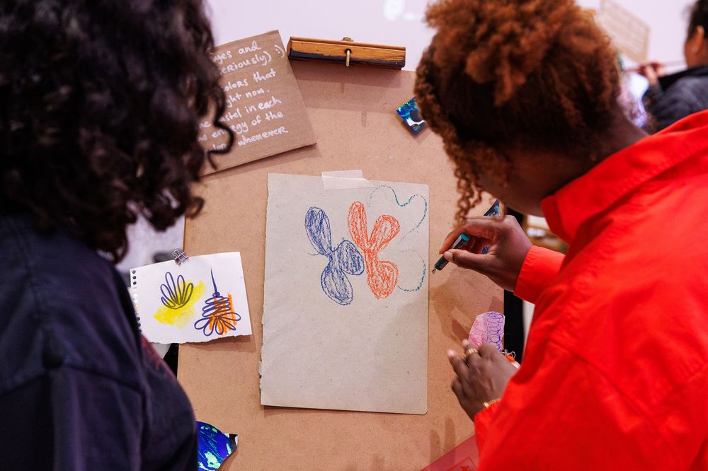 Two people leaning over a table examining colorful abstract drawings on brown paper at an art workshop.