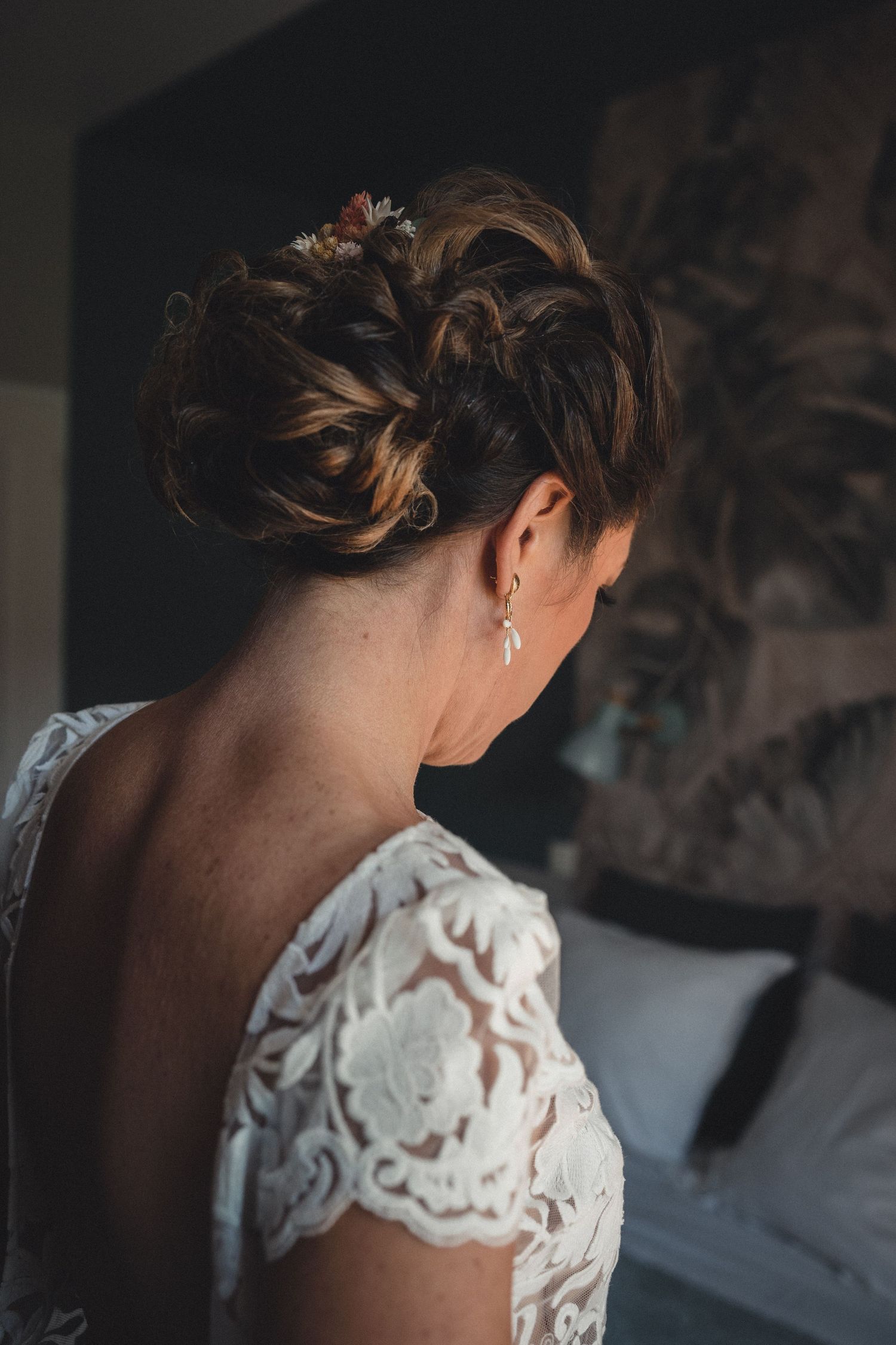 Bride with elegant braided updo hairstyle and pearl drop earring wearing a lace wedding dress.