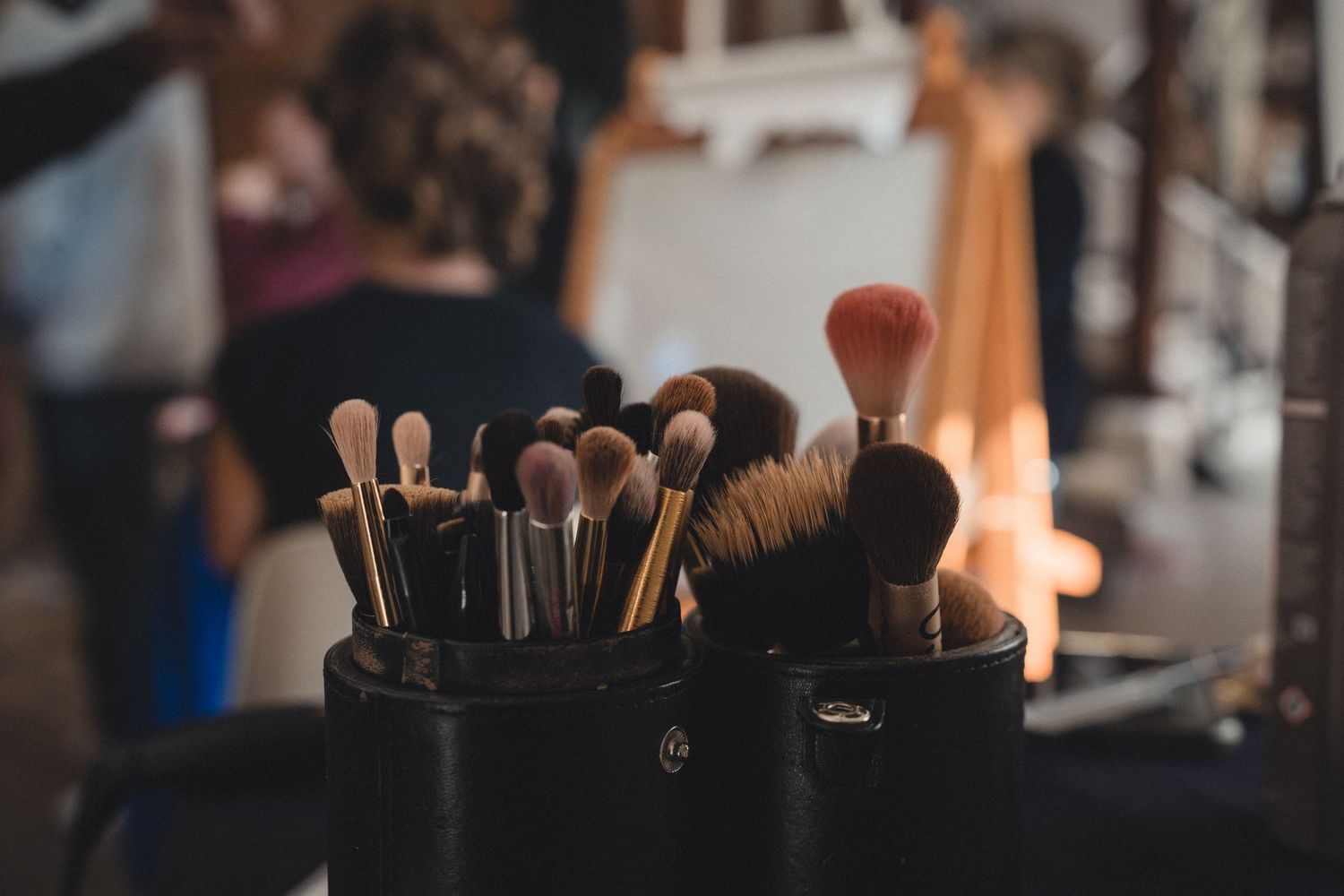 Two black containers filled with assorted professional makeup brushes on a vanity table in a beauty studio.