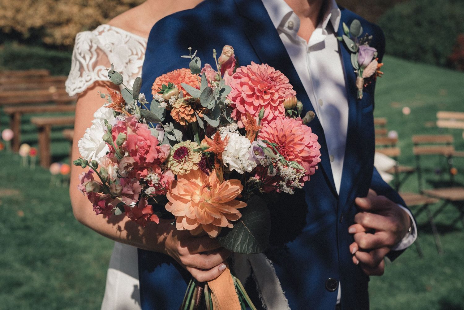 Bride and groom hold a vibrant wedding bouquet of pink dahlias and eucalyptus at an outdoor ceremony.