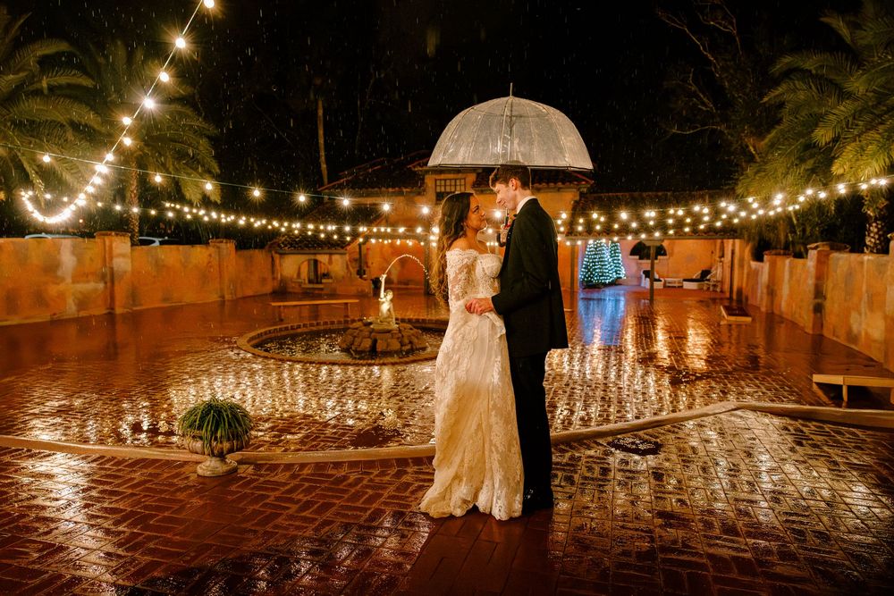 Bride and Groom in rain, with hanging lights on terrace with clear bubble umbrella at the Howie Mansion in Florida