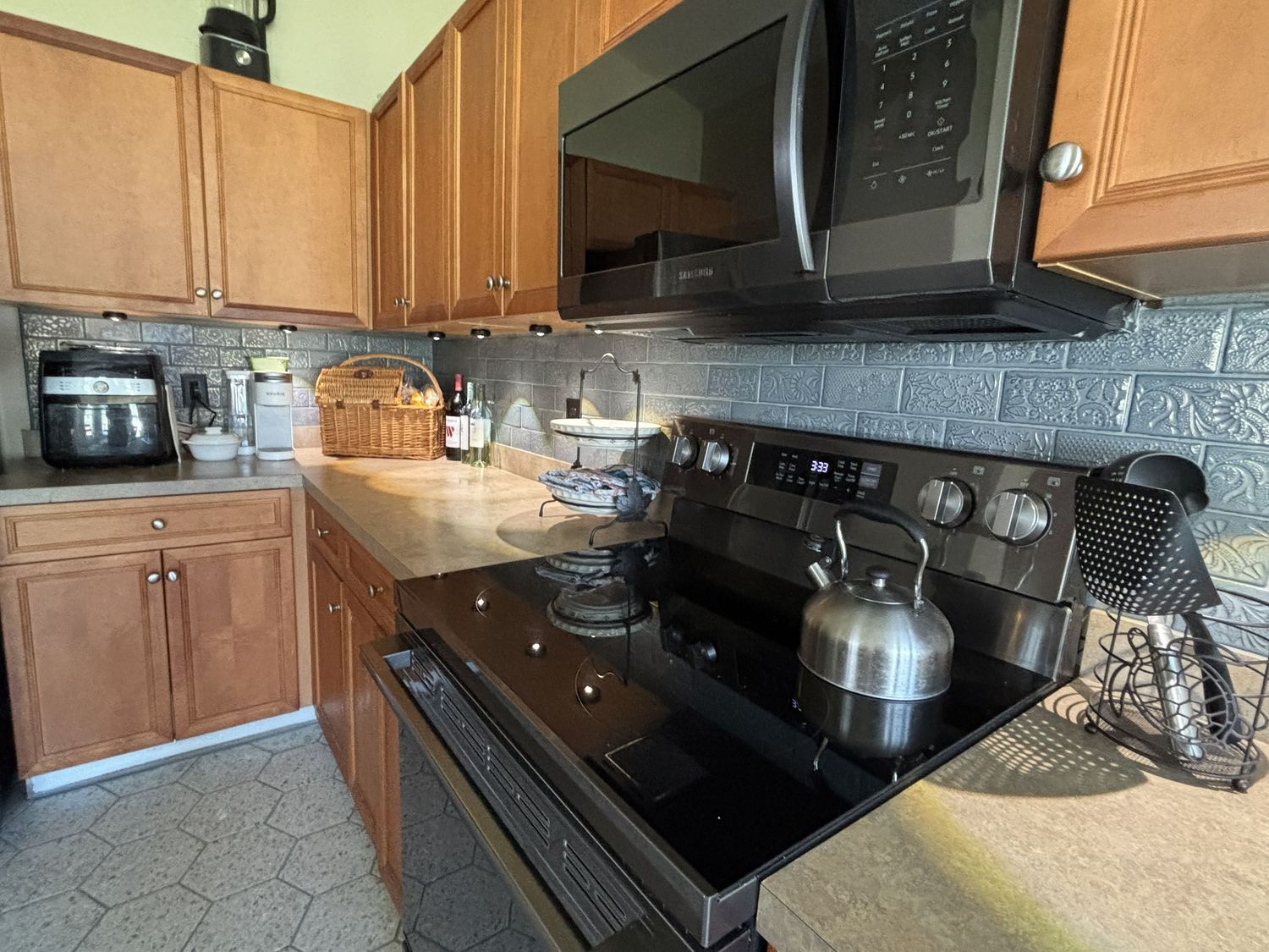 Modern kitchen with black appliances, granite countertops, tile backsplash, and wood cabinets.