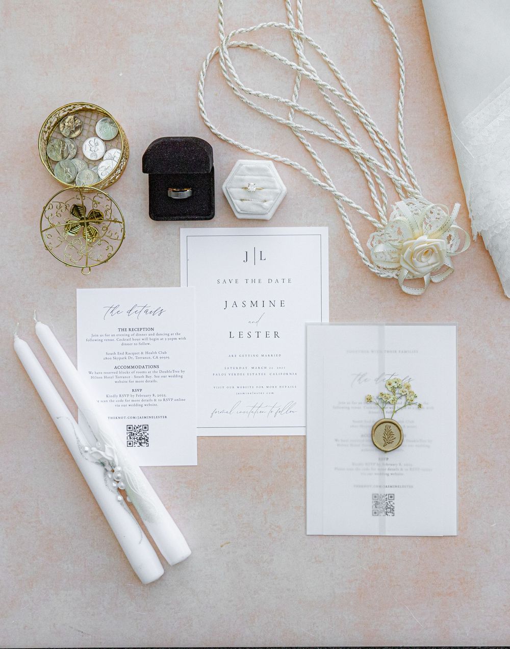 Elegant wedding invitation suite with save the date cards, ring boxes, white taper candles, and rope accents on a soft pink background.