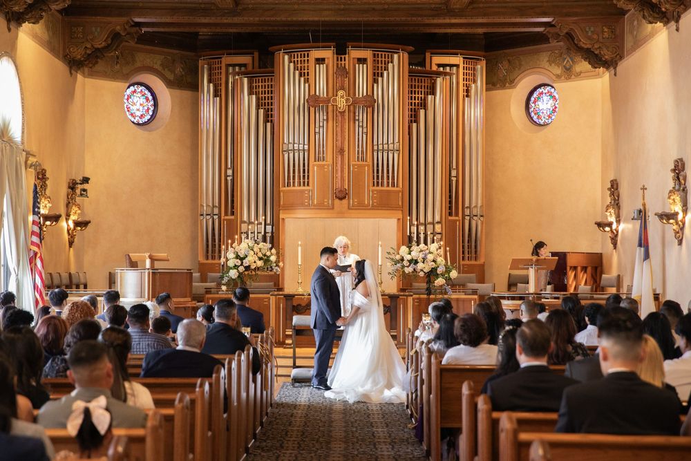 Bride and groom share first kiss at elegant church altar with grand pipe organ backdrop.