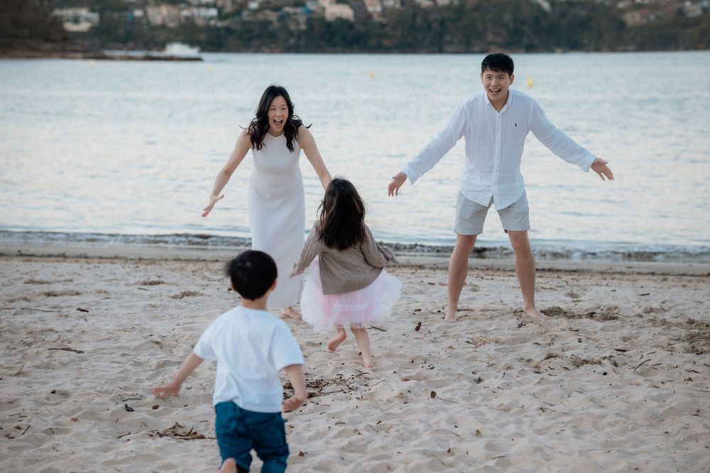 Family of four joyfully running toward each other on a sandy beach at sunset, children embracing parents in a heartwarming reunion.