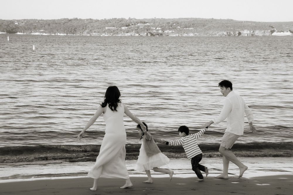 Black and white photo of a family holding hands and playing on a beach near the water.