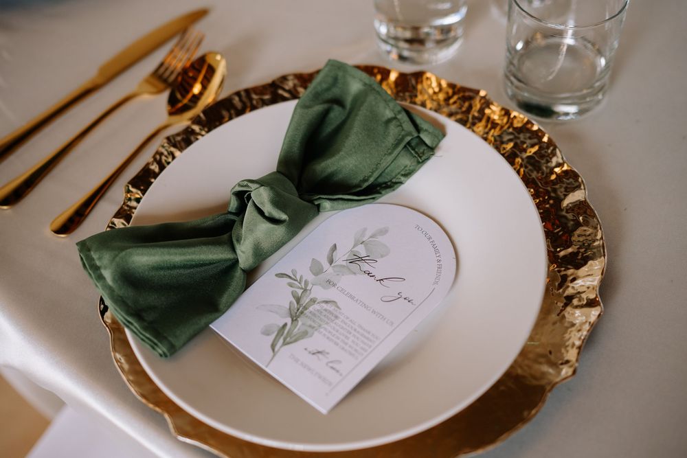 Elegant wedding place setting with gold charger plate, green velvet bow napkin, floral menu card, and gold cutlery.