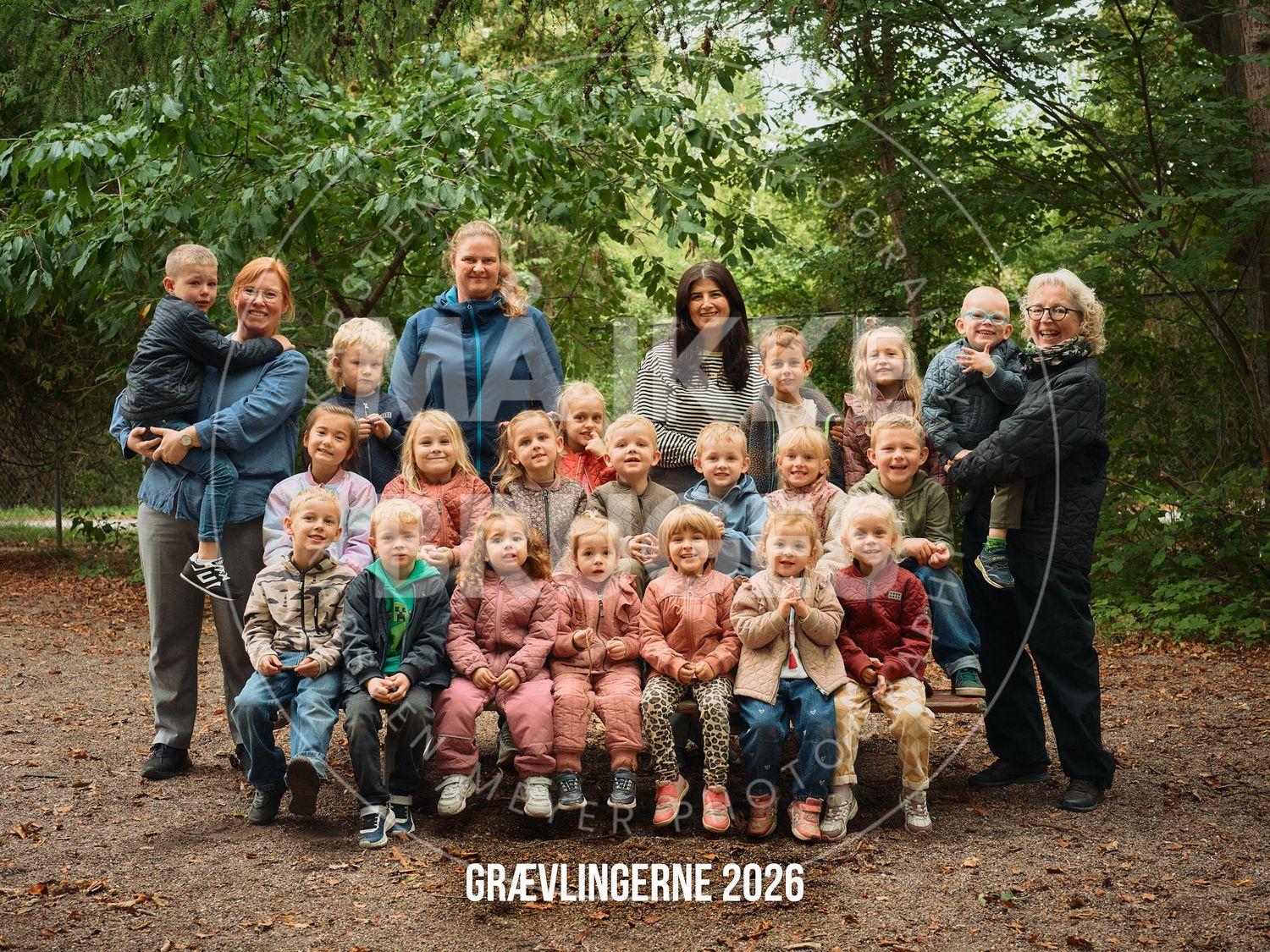 Group photo of children and teachers at Grævlingerne 2026 daycare, posing outdoors among green trees.