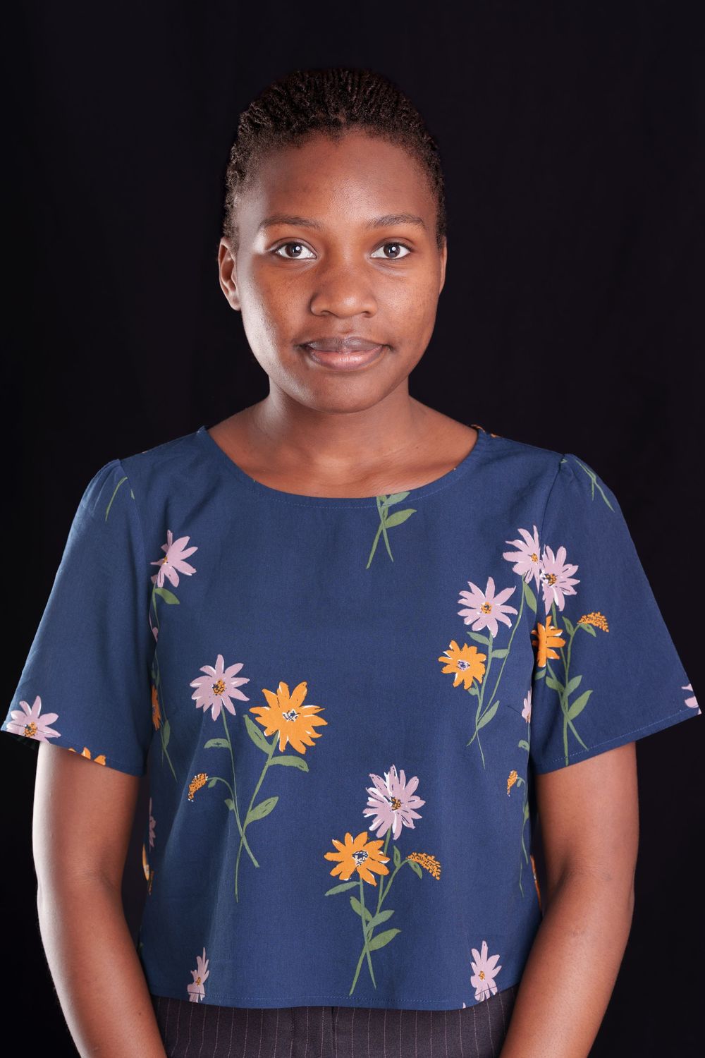 Young woman in blue floral top posing against black studio background.