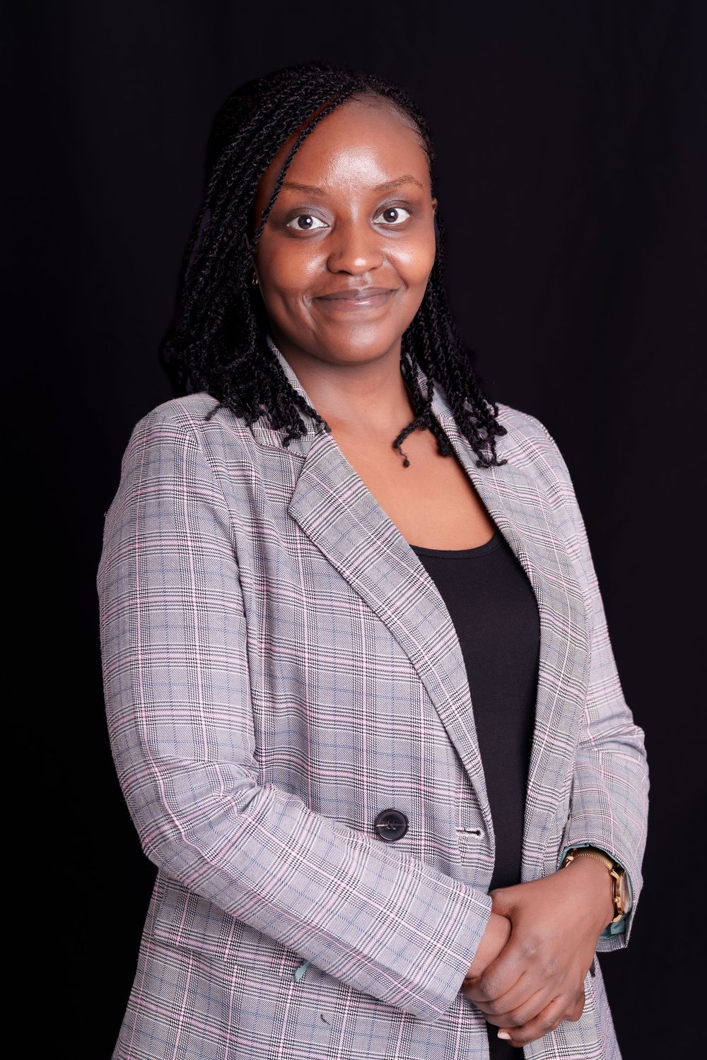 Professional woman in grey plaid blazer smiling against black studio background.