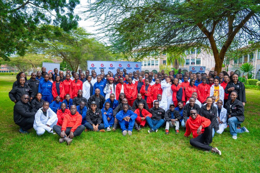 Large group of athletes in red and blue sportswear pose for team photo on green lawn outdoors.