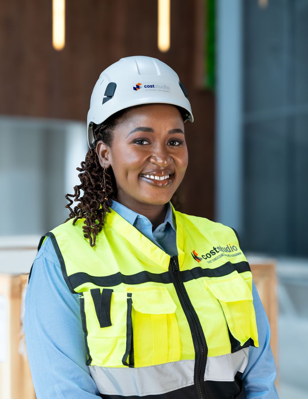 Happy African woman in yellow safety vest and white hard hat smiles at construction site.