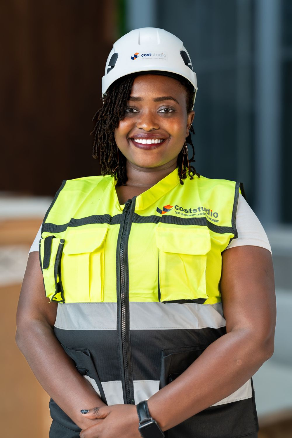 Smiling African woman in Coststudio yellow safety vest and white hard hat at construction site.