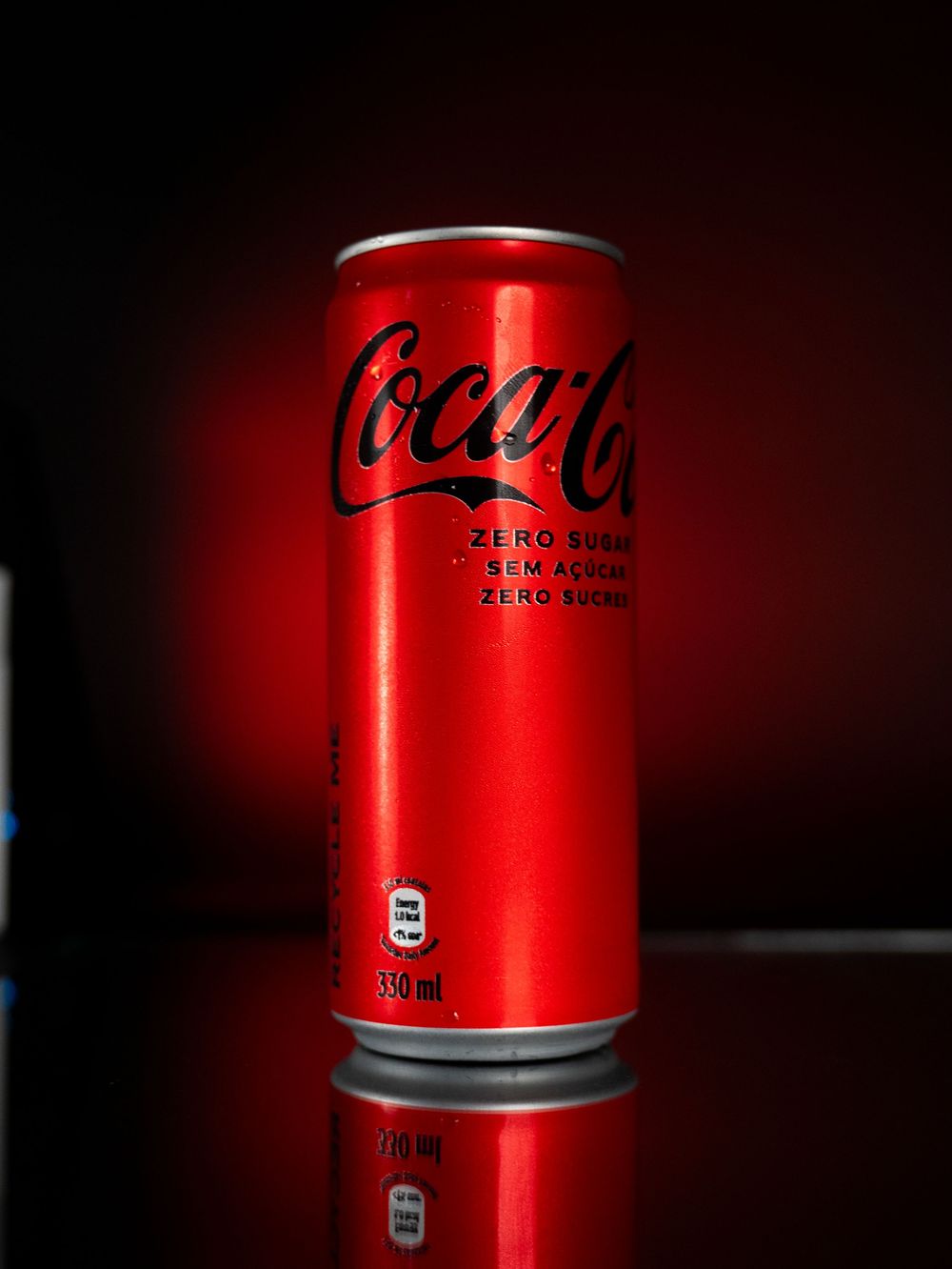 Coca-Cola Zero Sugar slim red can on reflective dark surface with red lighting.