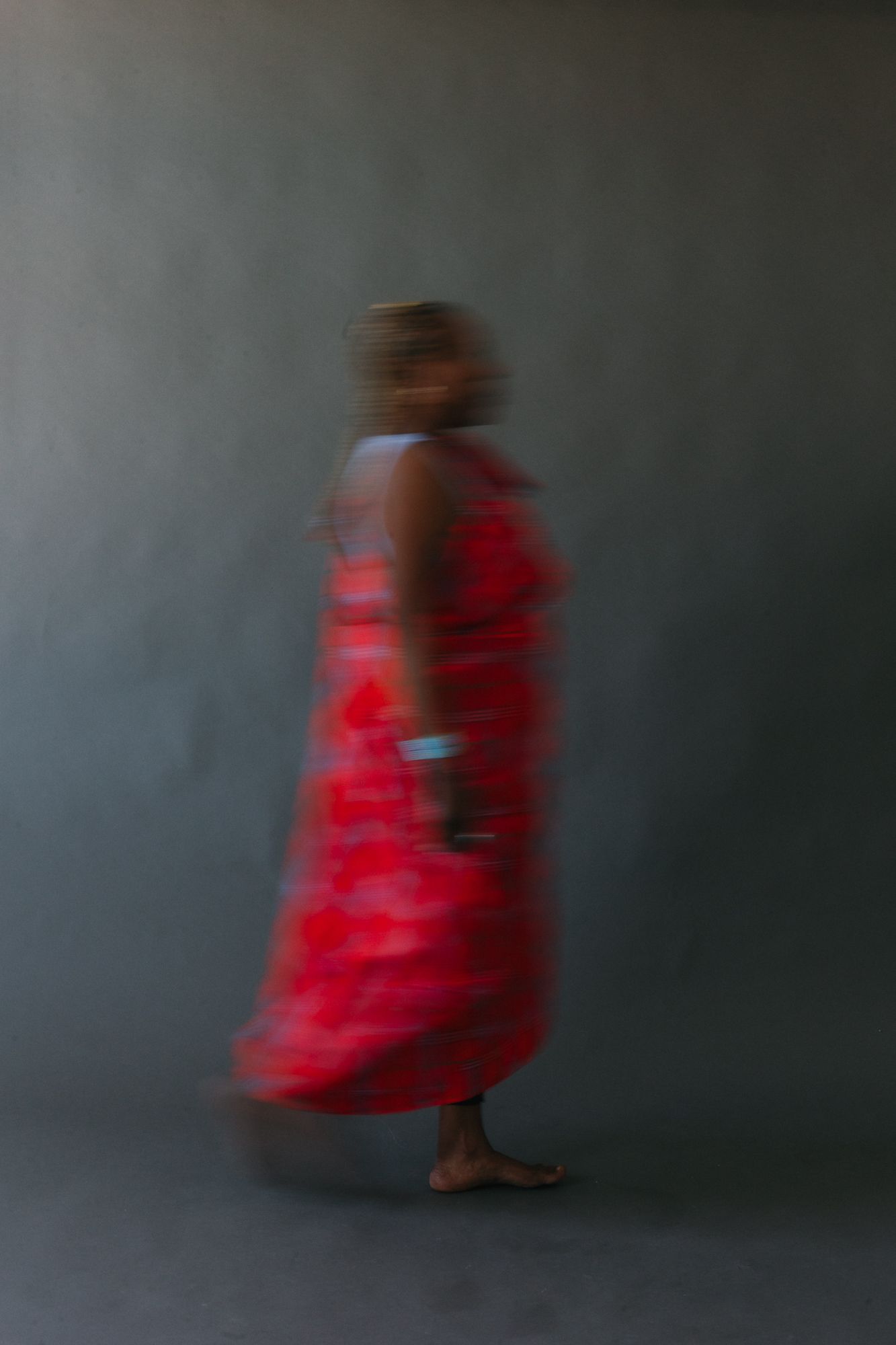 Blurred motion photo of a person in a vibrant red dress walking against a gray background.