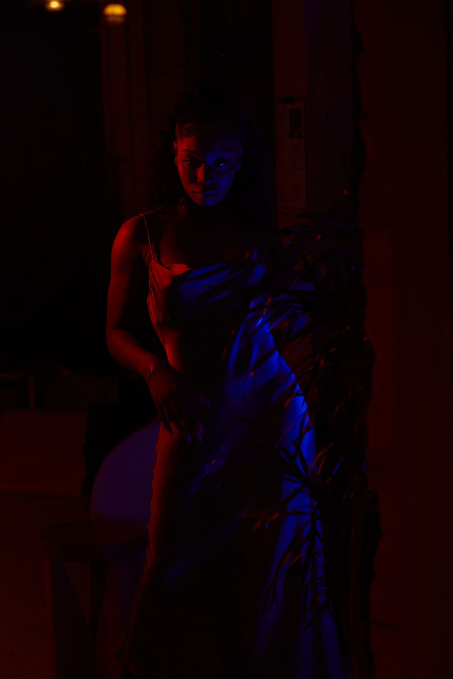Woman in a saree posed dramatically under red and blue neon lights in a dark atmospheric setting.