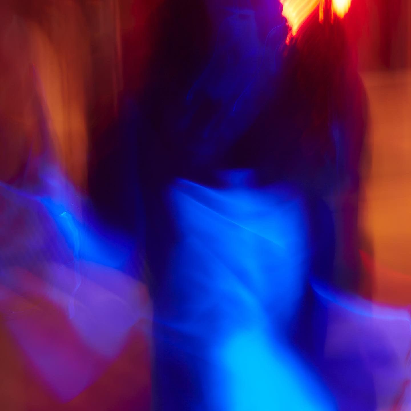 Abstract motion blur of dancers under vibrant blue and red nightclub lights creating a dynamic, colorful effect.