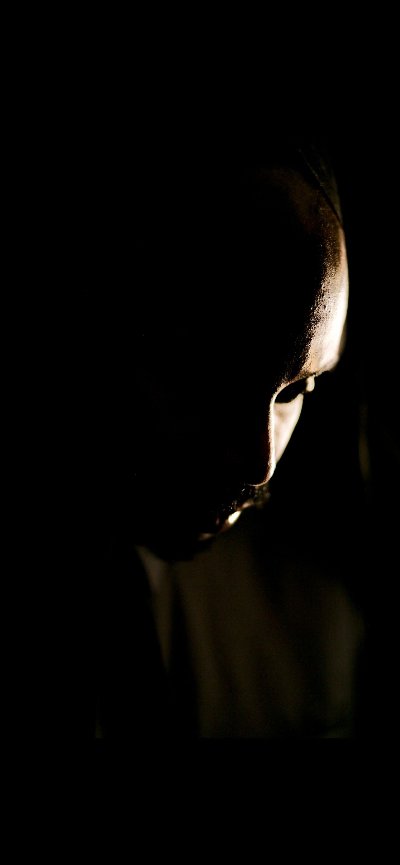 Dramatic low-key portrait of a person partially lit in darkness, showcasing moody chiaroscuro photography technique.