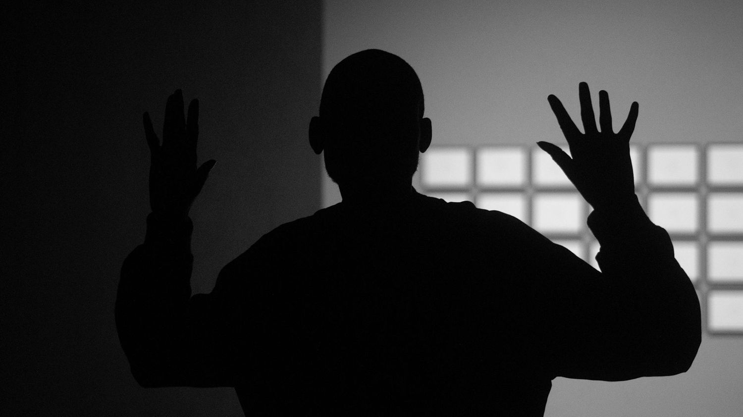 Silhouette of a man with hands raised against a bright window in a dramatic black and white photo.
