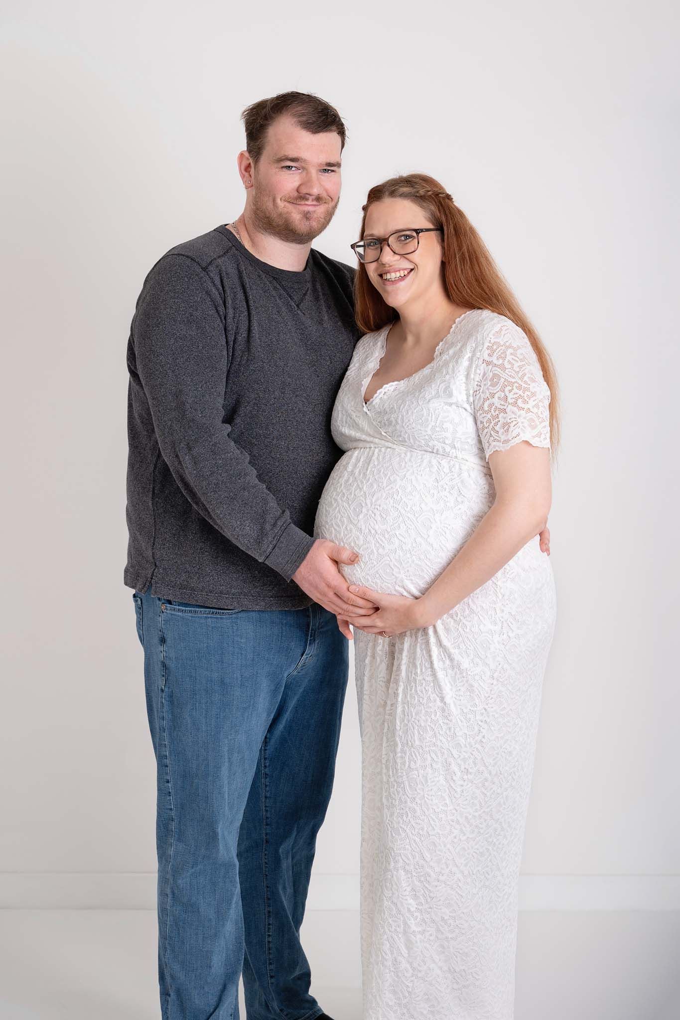 Pregnant mother sits with husband cuddling together in studio maternity session in Baltimore Ontario.