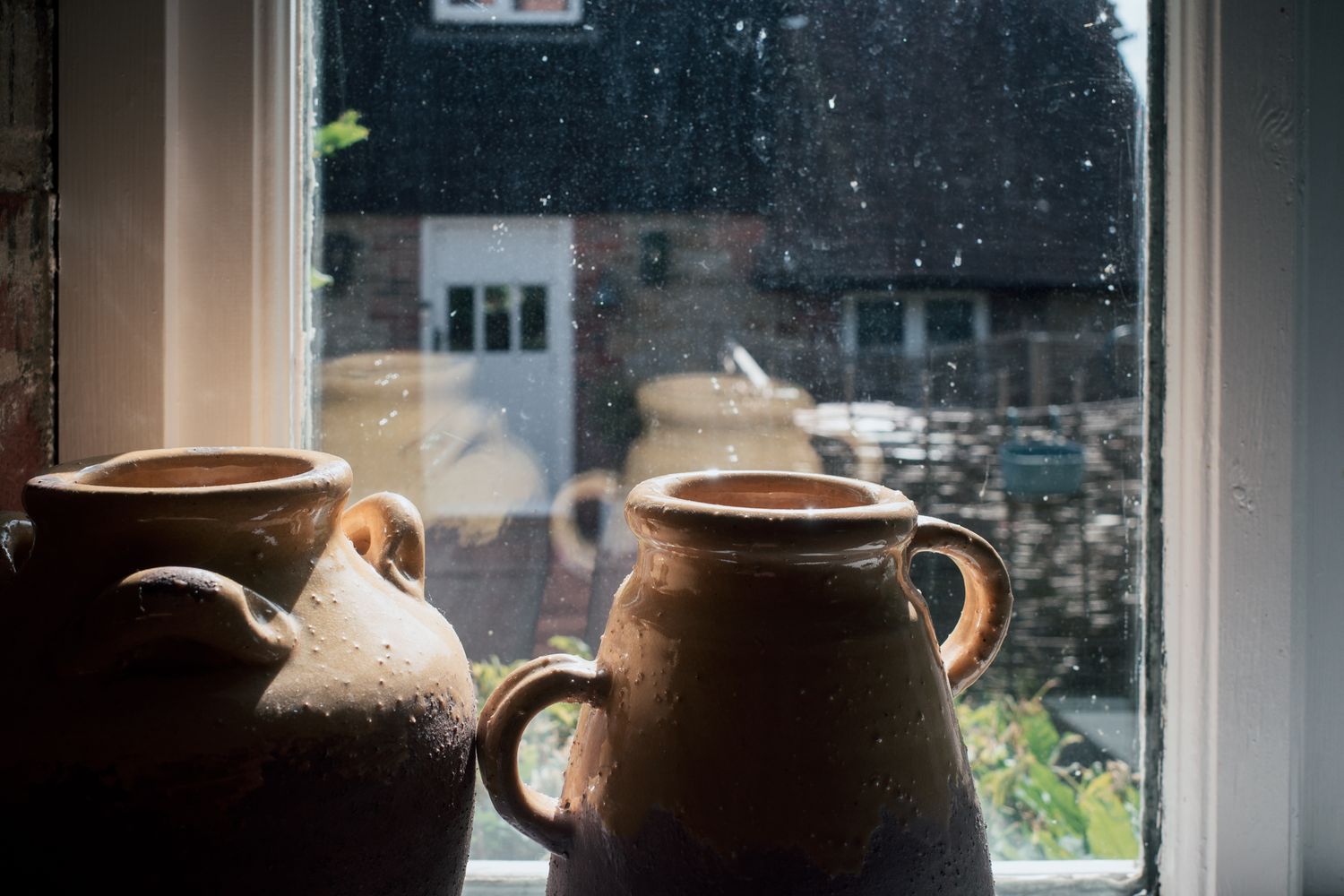 Rustic clay pottery jugs on a windowsill with a rainy street view in the background.