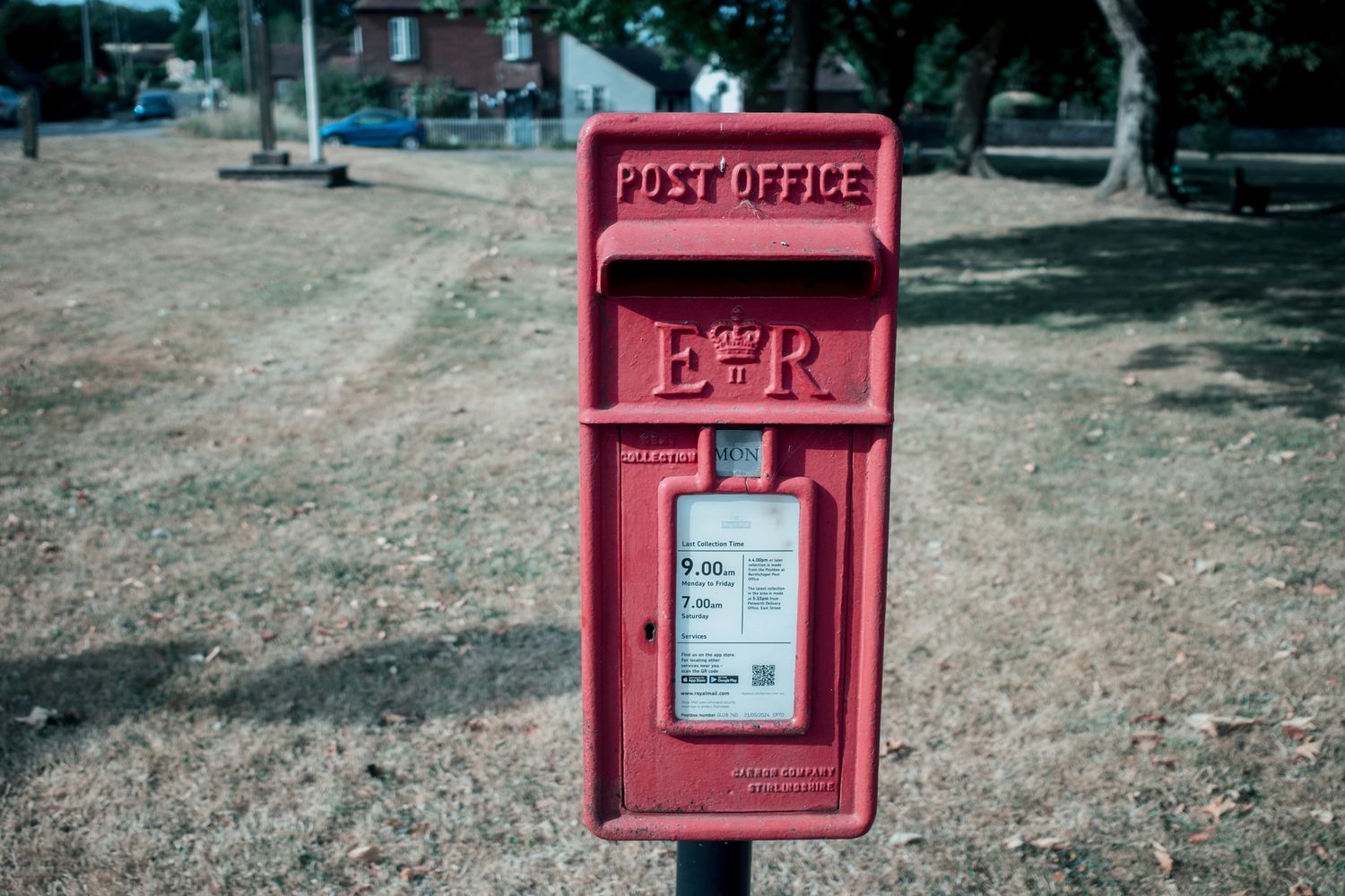 Red Royal Mail post office box with ER cipher on green grass background in the UK.