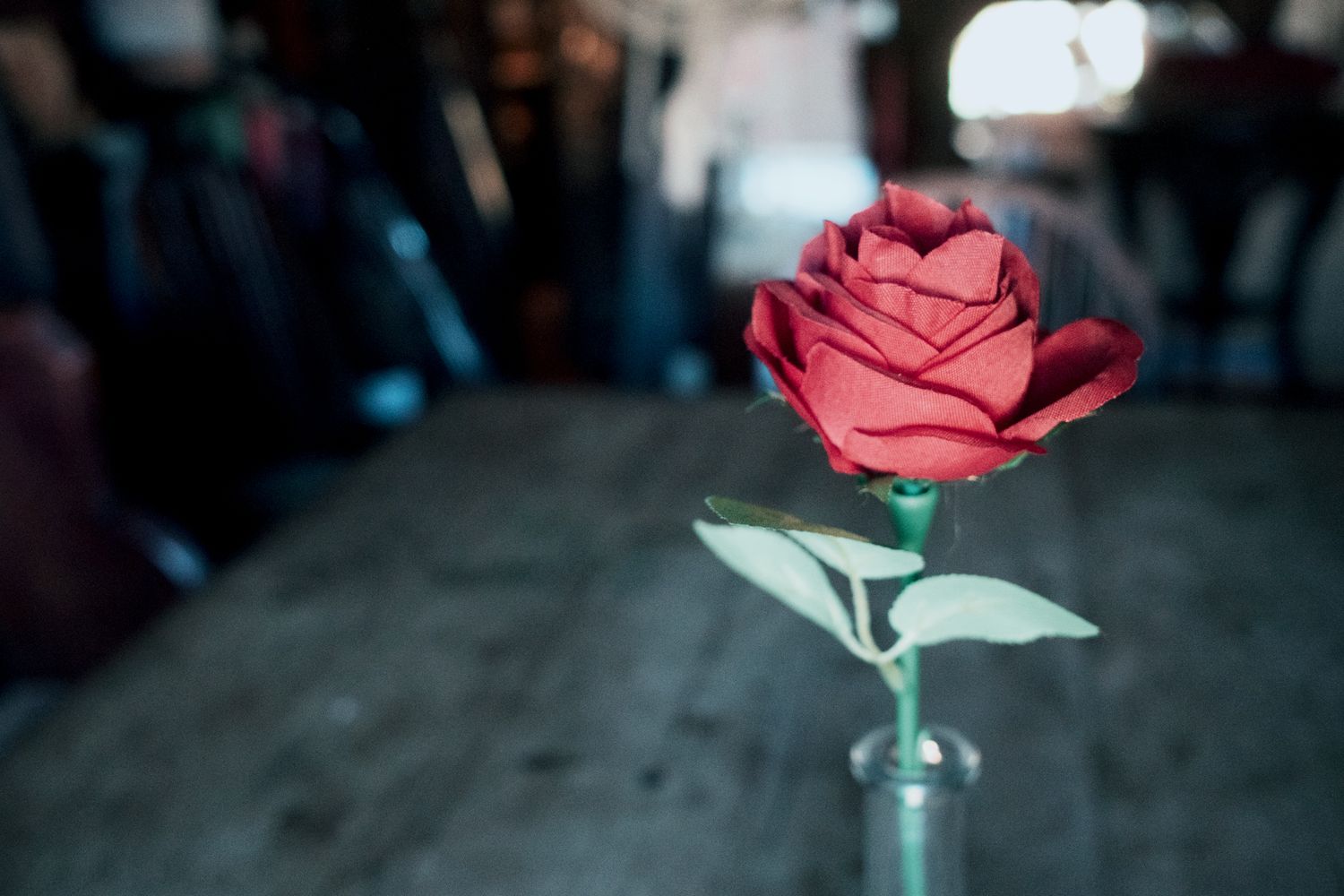 A vibrant red paper rose in a small vase on a wooden table with a blurred background.