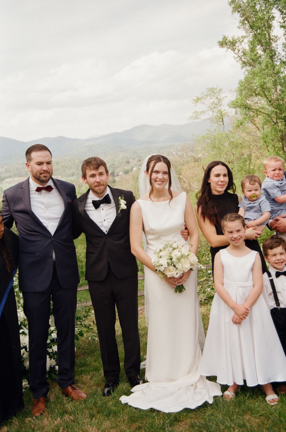 Wedding party poses with bride and groom against scenic mountain backdrop on spring wedding day.