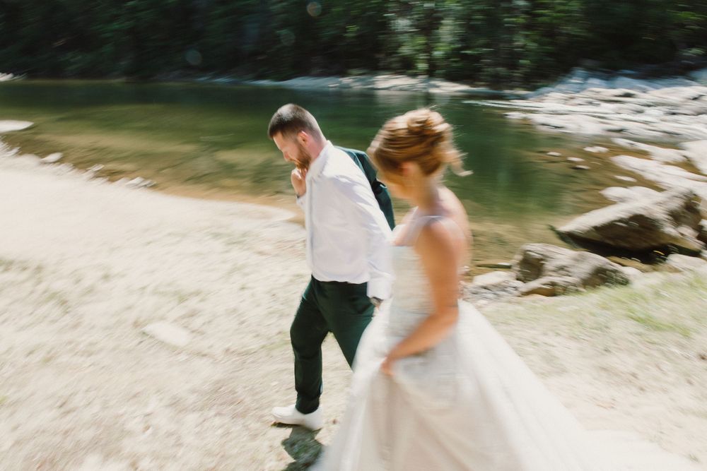 Bride and groom walking hand in hand along a scenic riverside, captured with motion blur on their wedding day.