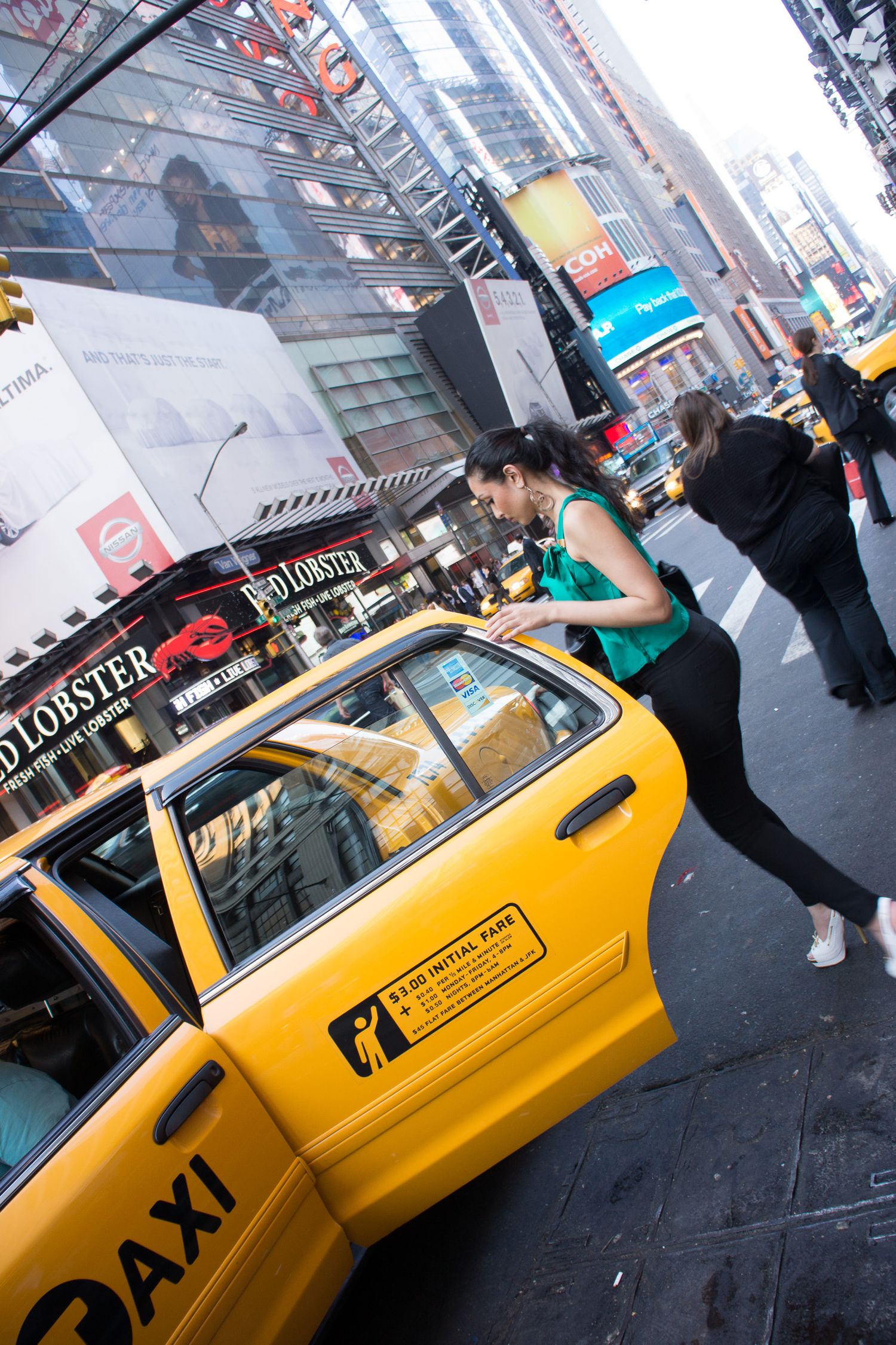 Woman in green top hailing a yellow NYC taxi cab near Times Square with Red Lobster sign visible.