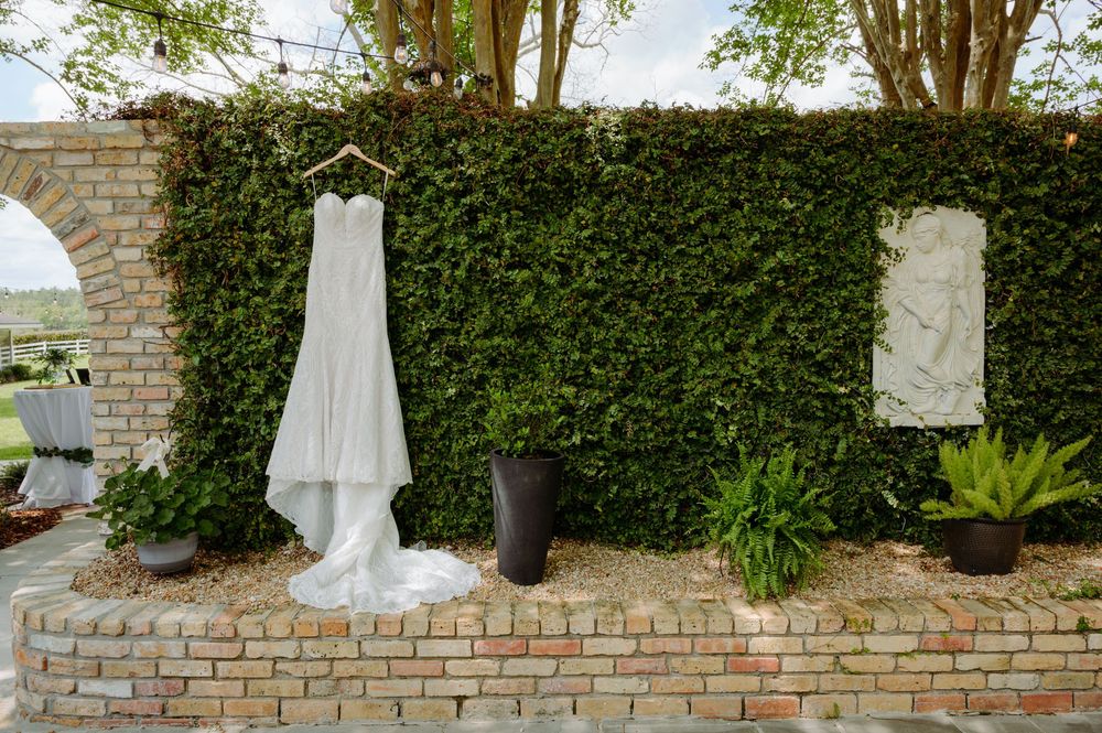 Elegant white wedding dress hanging on ivy-covered brick wall outdoors at wedding venue.