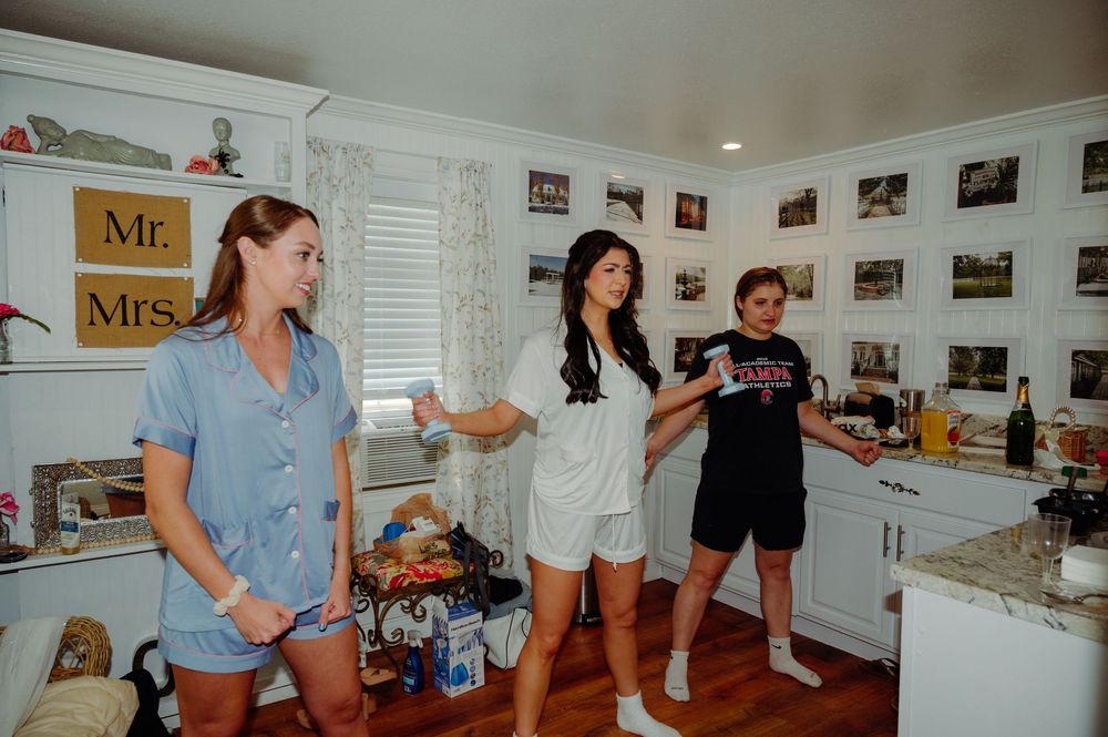 Three women socializing in a decorated kitchen with Mr. and Mrs. signs, photos on the wall, and marble countertops.