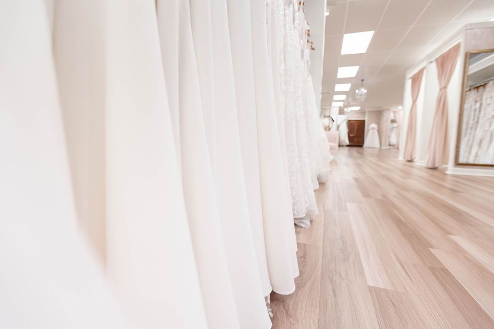 Rows of elegant white wedding dresses hanging in a bright bridal boutique with light wood floors.
