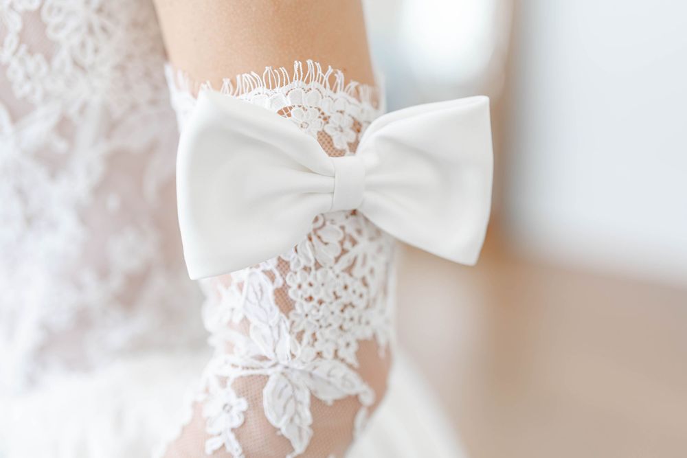 Close-up of a bridal lace garter with a white satin bow on a bride's arm