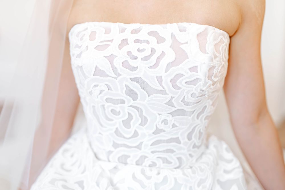 Close-up of a strapless white wedding dress with intricate floral lace applique detailing on the bodice.
