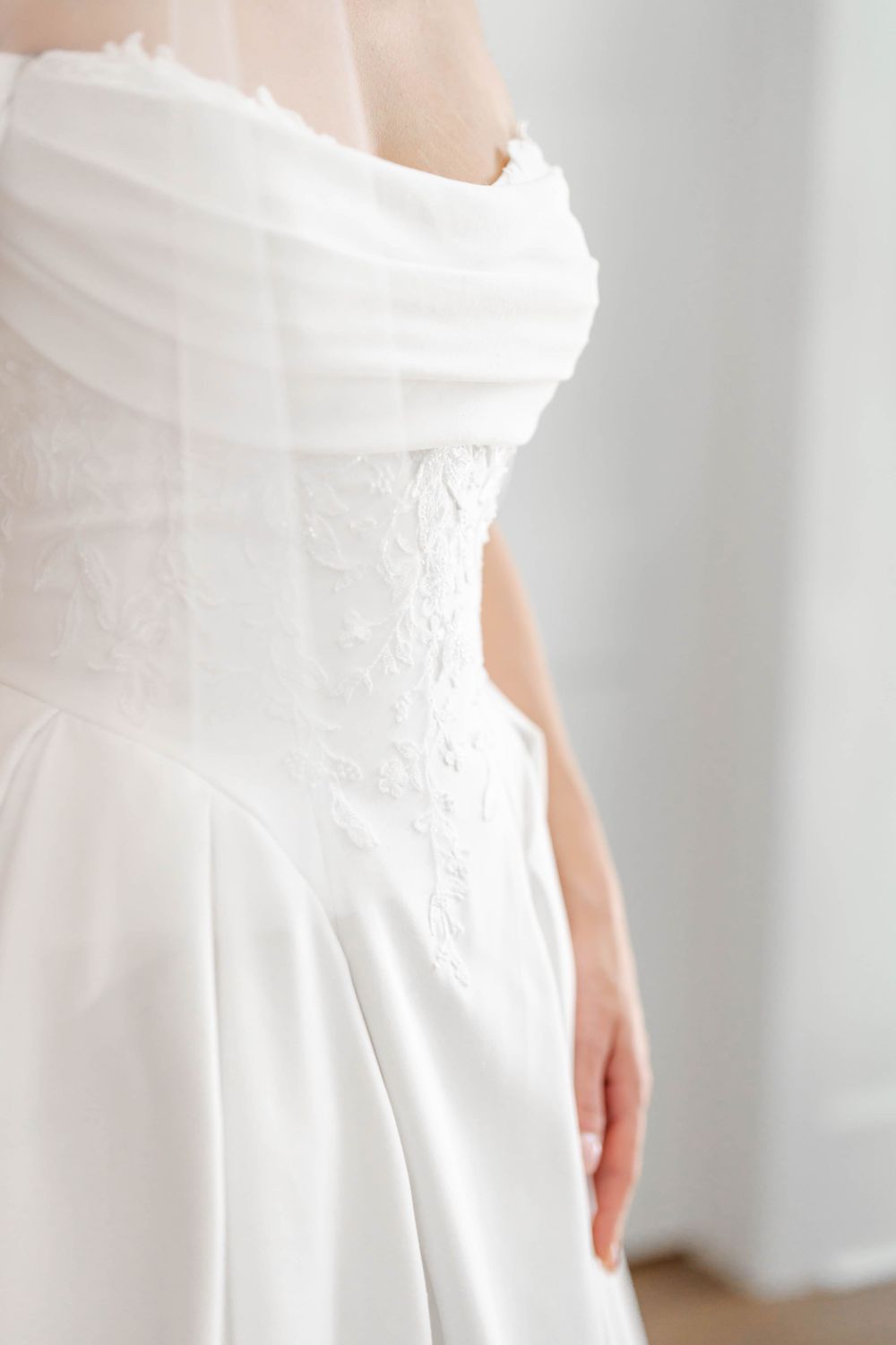 Close-up of a bride in a white strapless lace corset wedding gown with flowing satin skirt and sheer veil.