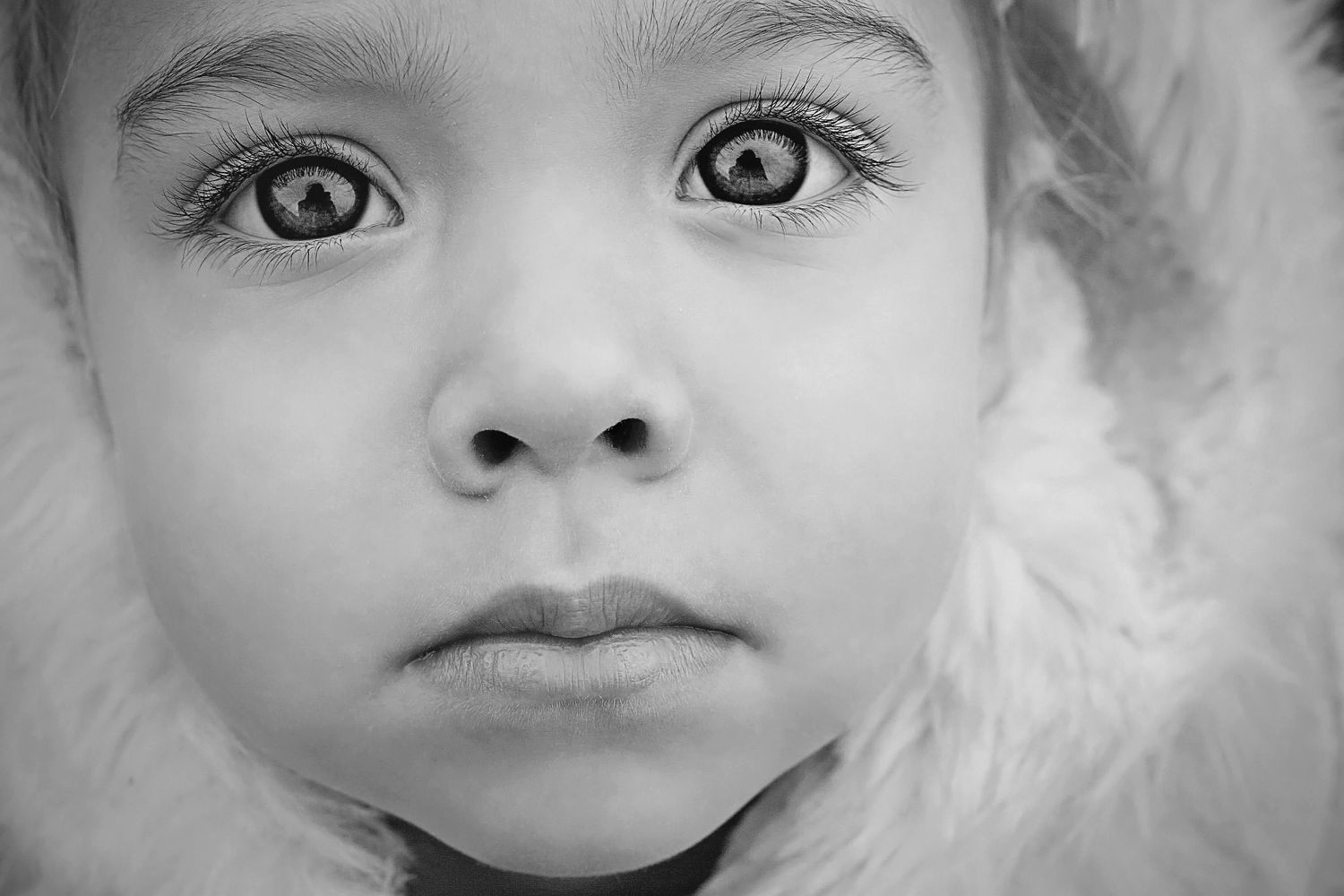 Black and white close-up portrait of a young child with big wide eyes and a fur-trimmed hood.