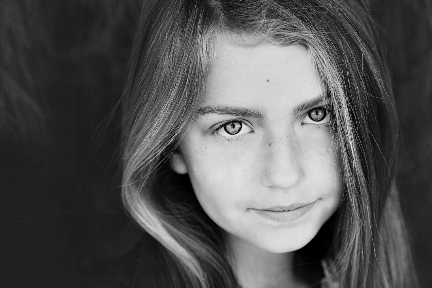 Black and white close-up portrait of a young girl with long hair and light eyes gazing softly at the camera.