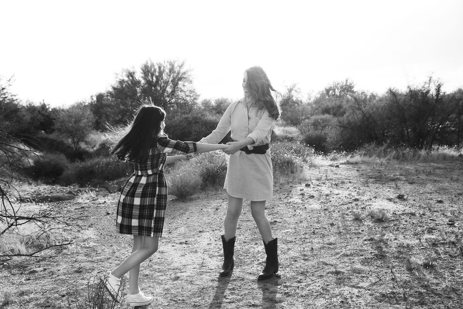 Black and white photo of two girls holding hands and spinning playfully in a sunlit desert field.