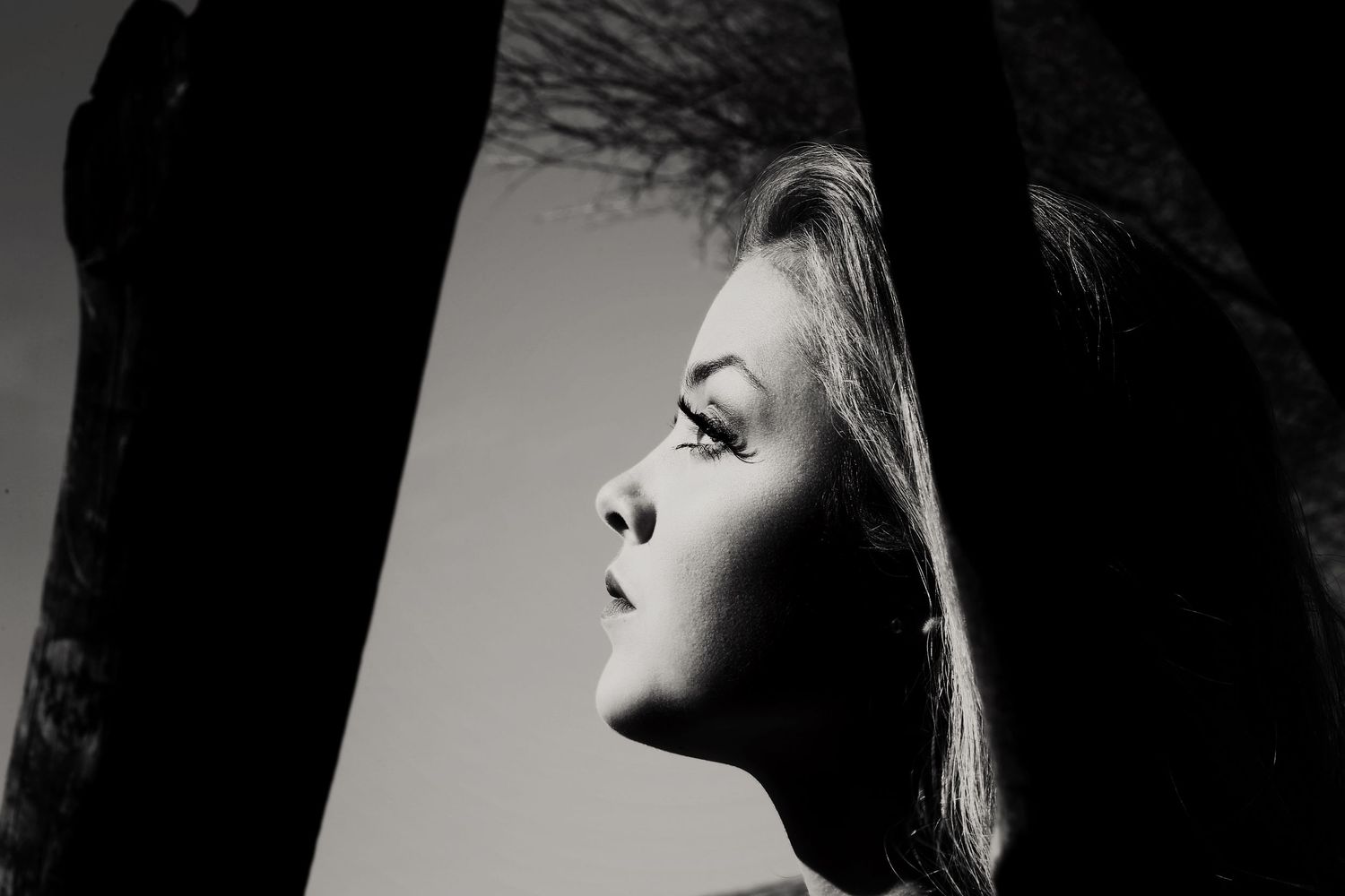 Black and white side profile portrait of a young woman with long hair looking upward, framed by dark silhouetted shapes.