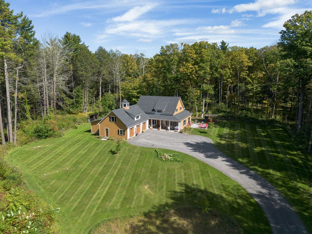 Aerial view of a charming country home surrounded by lush green lawn and dense forest trees.