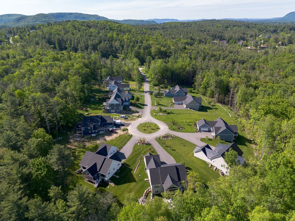 Aerial view of an upscale residential cul-de-sac neighborhood with elegant homes surrounded by green forest.