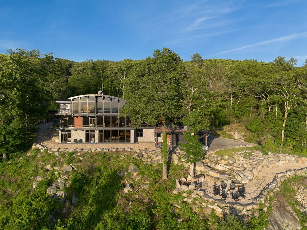 Aerial view of a modern cliffside home with large windows nestled among rocky terrain and trees.