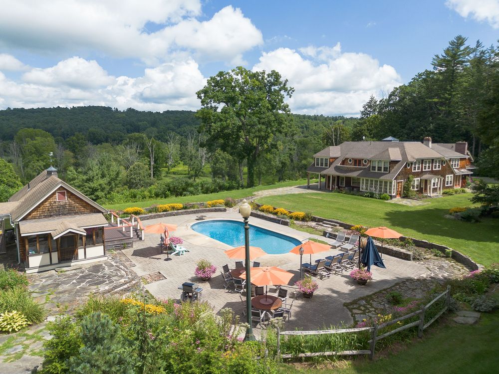Aerial view of an elegant estate with an outdoor swimming pool, patio, and manicured gardens.