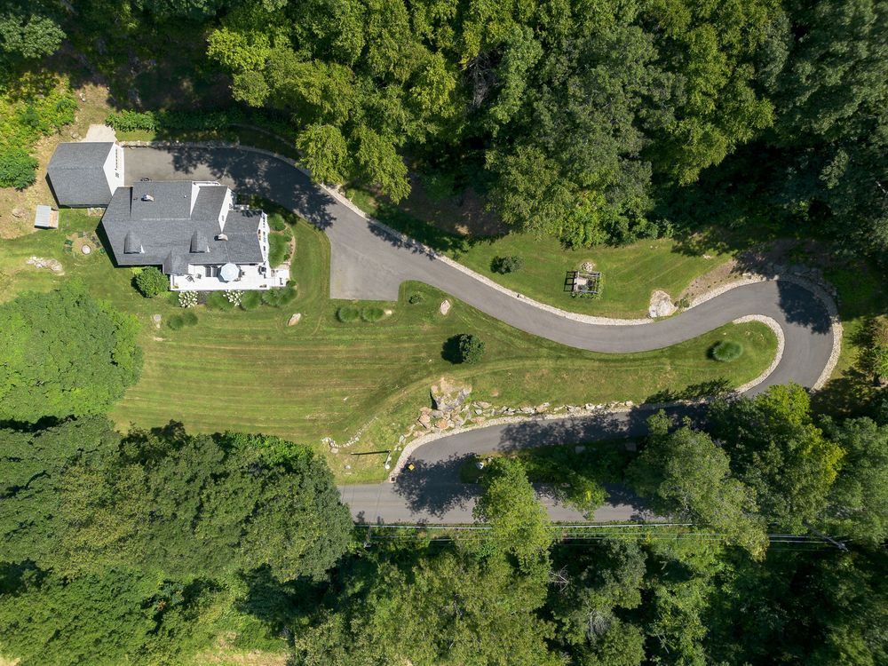 Aerial view of a white country estate with a winding driveway surrounded by lush green trees.