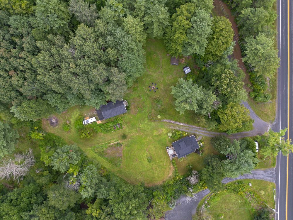 Aerial top-down view of small rural cabins nestled within a dense evergreen forest roadside.
