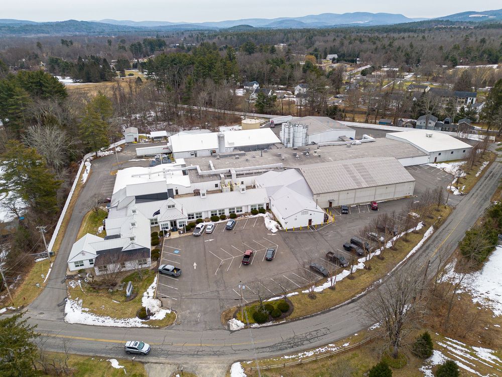 Aerial view of a large commercial facility with parking lot surrounded by a small New England town.