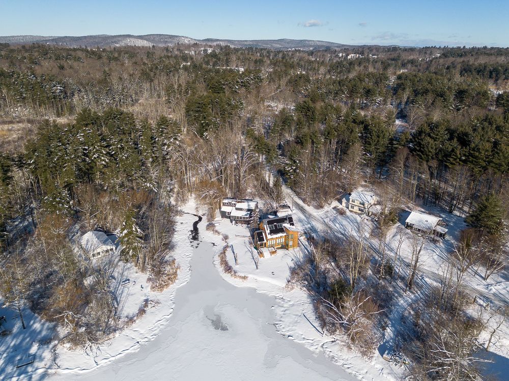 Aerial winter view of a rural property with frozen pond and snow-covered trees and landscape.