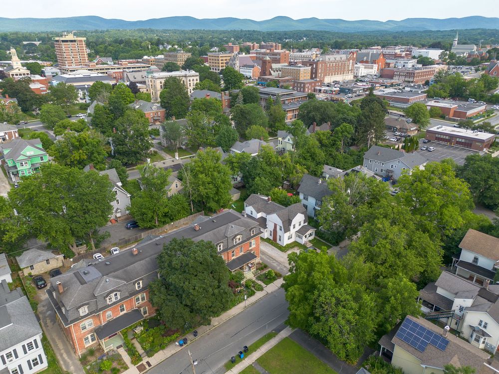 Aerial view of a charming small-town neighborhood with tree-lined streets and historic buildings and mountains beyond.